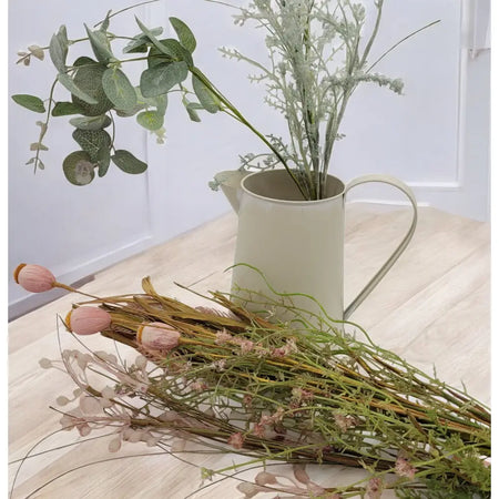 Vintage cream metal jug made of metal holding greenery and dried flowers with a handle