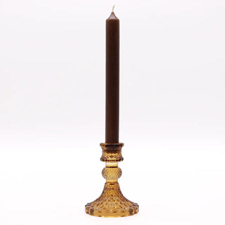 A tall brown candle in a faceted amber glass vintage dinner candle holder with intricate cut patterns for candles