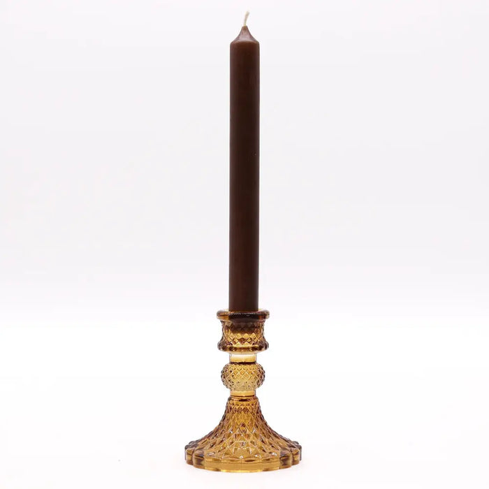 A tall brown candle in a faceted amber glass vintage dinner candle holder with intricate cut patterns for candles