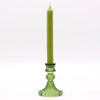 A tall olive green candle in a vintage glass candle holder with intricate cut glass detailing for candles display