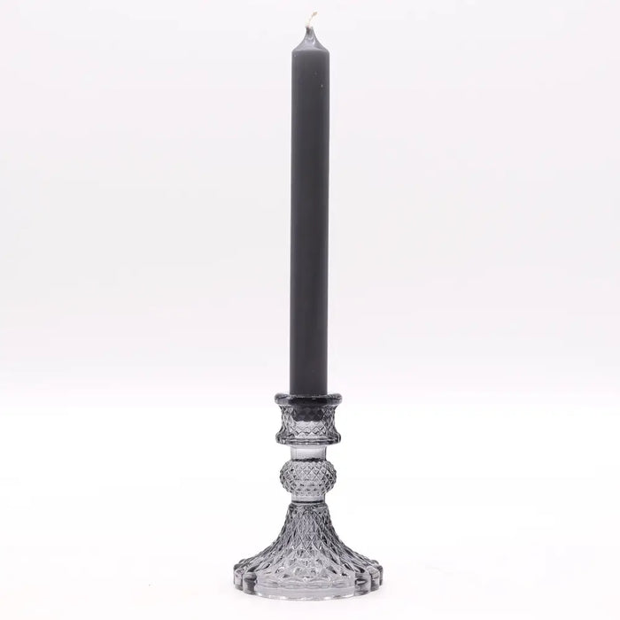 A tall sleek black candle sits in a clear crystal vintage dinner candle holder with intricate faceted patterns