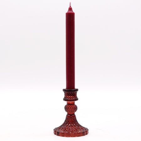 A tall deep red vintage dinner candle in a matching faceted glass holder with geometric patterns