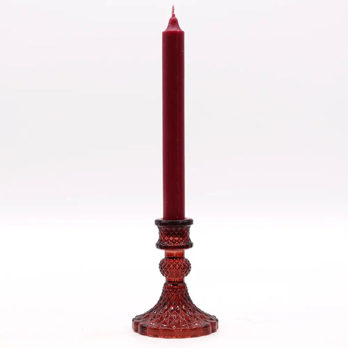 A tall deep red vintage dinner candle in a matching faceted glass holder with geometric patterns