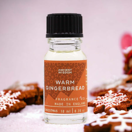 A clear glass bottle with black cap holds warm gingerbread fragrance oil labeled ancient wisdom made in england with allergen declarations