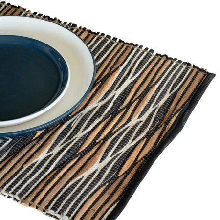 Handwoven water hyacinth placemat with textured black white and natural brown stripes in white waves pattern