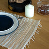 Beige woven water hyacinth placemat with frayed edges and textured striped pattern in natural tiger style