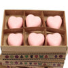 Six soft pink heart-shaped wax melts made of palm waxes arranged in a brown cardboard box with patterned tape