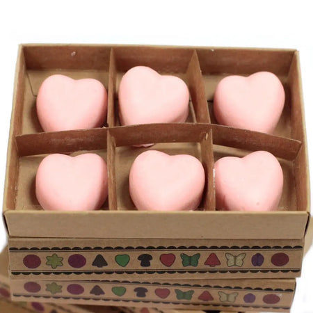 Six soft pink heart-shaped wax melts made of palm waxes arranged in a brown cardboard box with patterned tape