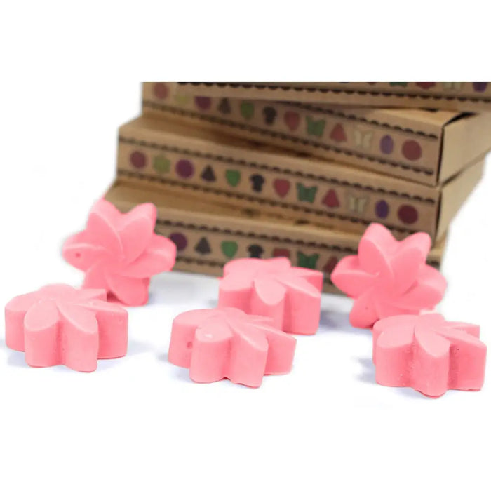 Pink flower-shaped wax melts made from palm waxes scattered in front of stacked cardboard boxes for japanese magnolia