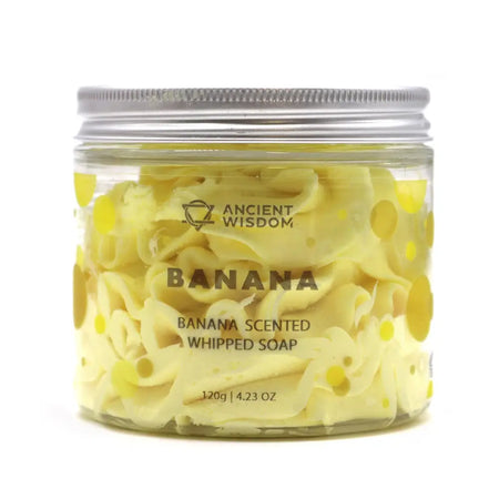 A clear glass jar with a silver lid holds pale yellow whipped soap scented with banana weighing 120g
