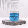 A clear glass jar with silver lid holds vibrant blue whipped soap with darker blue speckles labeled blueberry blast by ancient wisdom