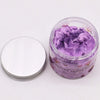 A clear glass jar with silver lid holds purple glittery whipped soap bath scrub labeled roasted sugar plum frosted sugar plum