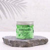 A translucent green jar of whipped soap with white tea scent and silver lid featuring a swirling bubble design