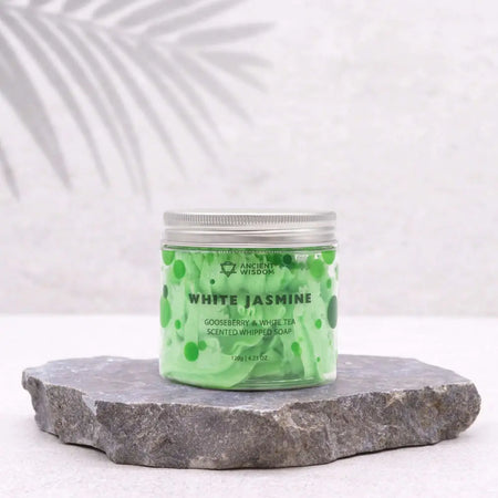 A translucent green jar of whipped soap with white tea scent and silver lid featuring a swirling bubble design