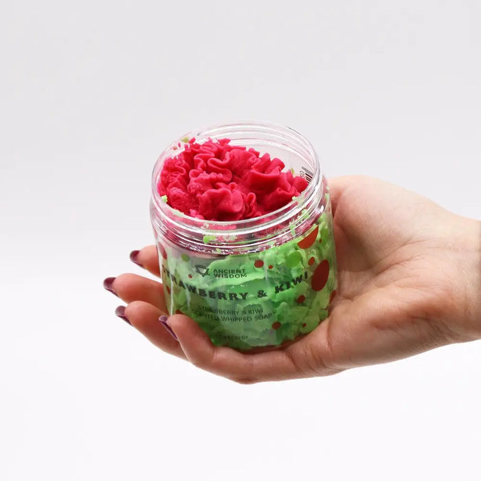 A clear glass jar of strawberry and kiwi scented whipped soap with fluffy pink swirls and fruit-themed labels