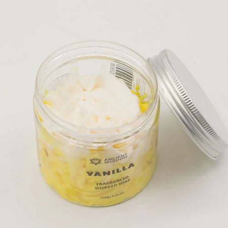 A clear glass jar with silver lid holds vanilla whipped soap with creamy white top and yellow base containing sodium cocoyl isethionate