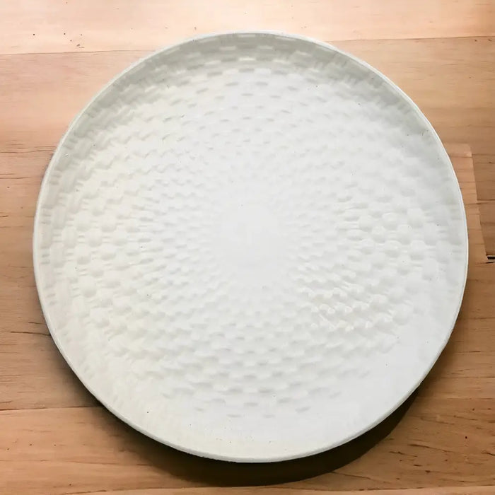 White ceramic plate with a textured hammered surface pattern on a round ceramic tray in white ceramic