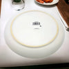 White ceramic plate with a subtle beige rim and a central barcode sticker featuring a weave design