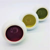 Three white ceramic tealight holders filled with deep red golden yellow and olive green liquids in a row