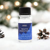 A clear glass bottle of white christmas fragrance oil with black cap and blue star label on snow beside pinecones