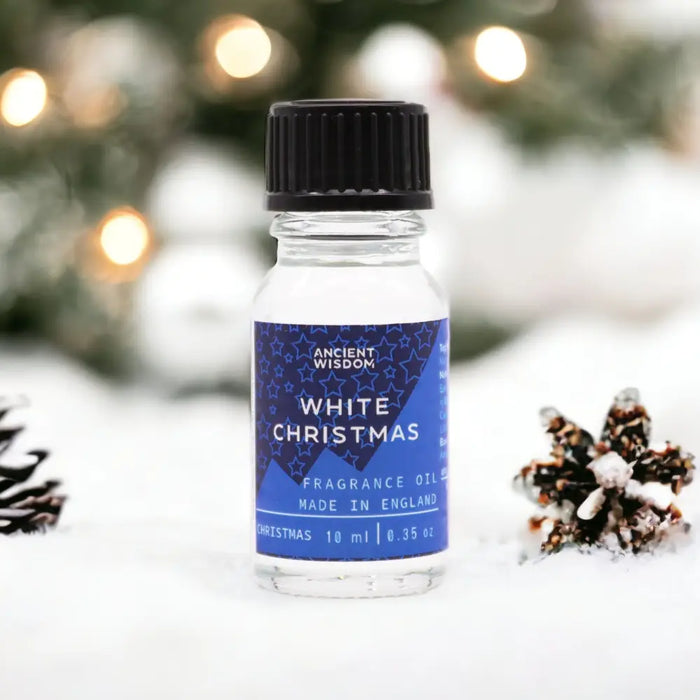 A clear glass bottle of white christmas fragrance oil with black cap and blue star label on snow beside pinecones