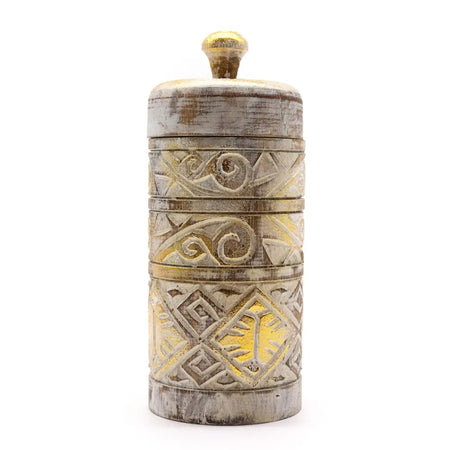 A white and gold wooden jar with intricate carvings and a golden knob on top in a rustic style