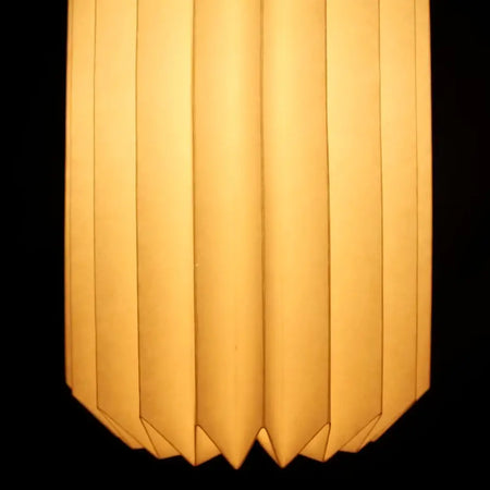 White origami paper lantern with warm vertical pleats and soft glowing light in a cylinder shape