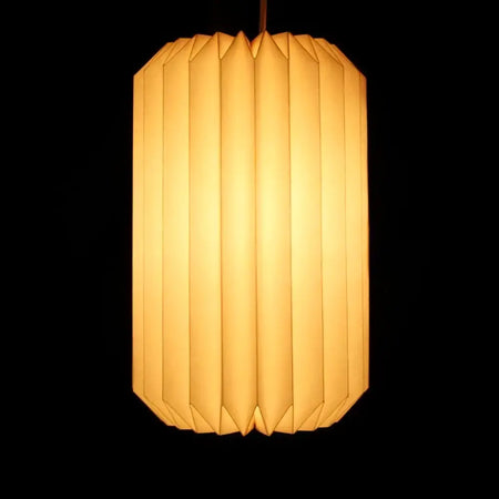 White origami light shade in a cylinder shape with warm, softly glowing paper and vertical pleats