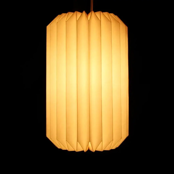 White origami light shade in a cylinder shape with warm, softly glowing paper and vertical pleats