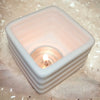 White porcelain tealight holder 6cm x 6cm with ribbed square design holding a lit porcelain tealight candle