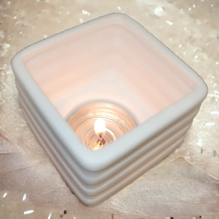 White porcelain tealight holder 6cm x 6cm with ribbed square design holding a lit porcelain tealight candle