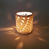 A warm cream-colored porcelain tealight holder with an intricate fern design made of porcelain material