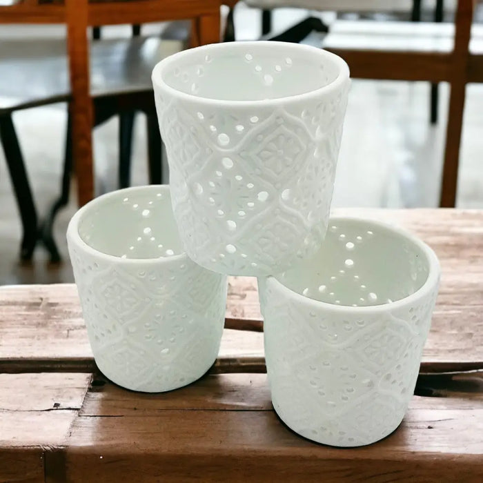 Three white porcelain tealight holders with intricate lace-like moroccan design cutout patterns