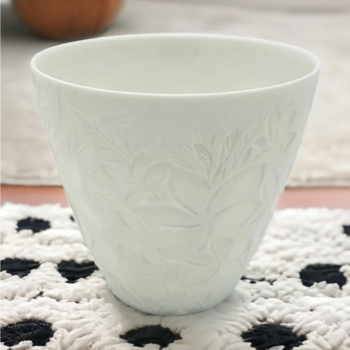 A white porcelain tealight holder with delicate embossed floral patterns in a frangipane design