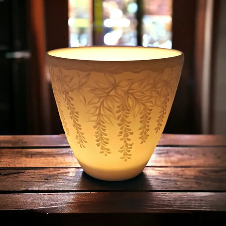 A warm glowing white porcelain tealight holder with delicate wisteria vine etchings