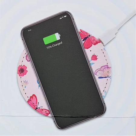 A pink floral wireless phone charging dock with a black samsung galaxy smartphone resting on it