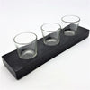 Black wooden block holding three clear glass votive and tealight holders on a rectangular tray