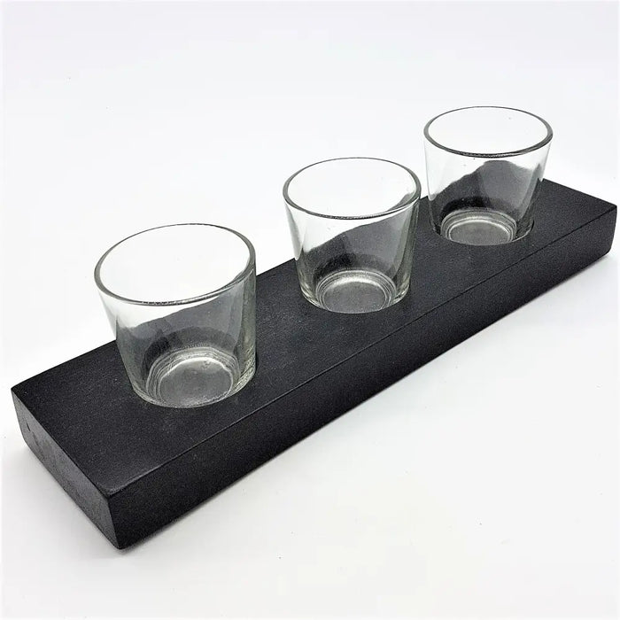 Black wooden block holding three clear glass votive and tealight holders on a rectangular tray