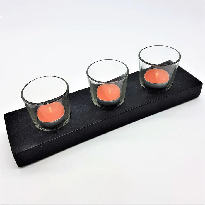 Black wooden block candle holder with three clear glass cups each holding coral colored tea lights