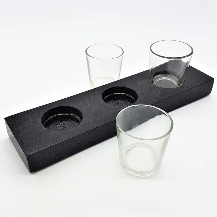 Black wooden block serving tray with three circular indentations holding clear glass votive tealight holders