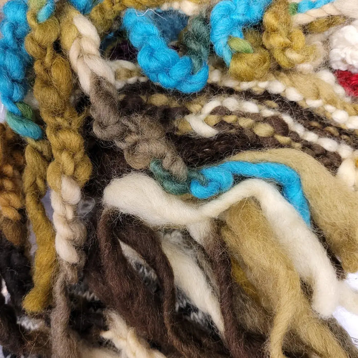 A wool hat with tassels flowers and plaits made from colorful hand dyed wool yarns in earthy tones and vibrant blues