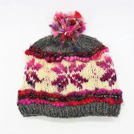 A hand-knitted wool and silk bobble hat with gray base cream and magenta flowers red pink bands and a multicolored pom-pom