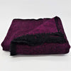 Folded woven woollen shawl and throw in purple and black with a herringbone pattern and fringed edges