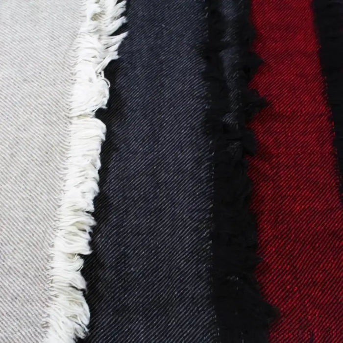 A close-up of woven woollen shawl swatches in light gray, dark navy denim, and red plaid with frayed edges