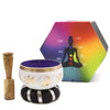 White singing bowl set with gold yin yang symbol and flower motifs on a black and silver cushion with wooden mallet