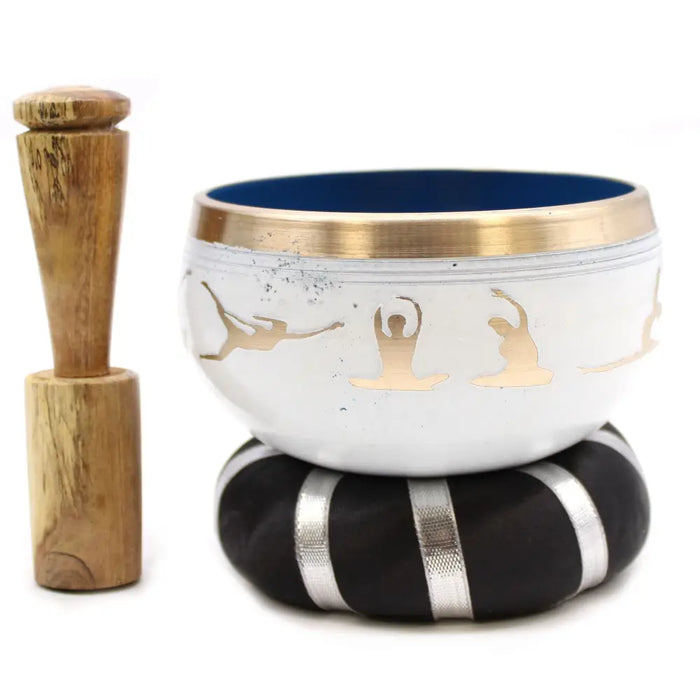 White singing bowl set with gold rim and engraved yoga moves designs resting on black cushion with silver stripes