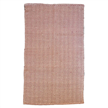 A rectangular woven cotton rug with a bold zig zag herringbone pattern in terracotta and cream colors