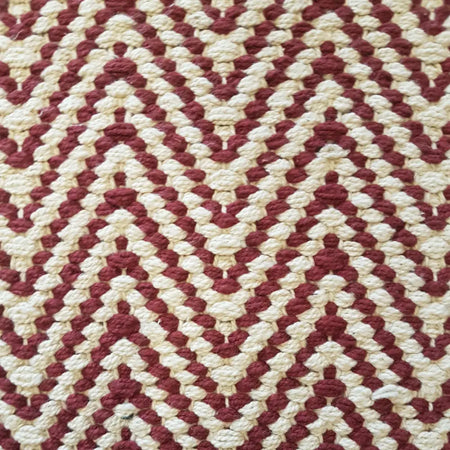 A handcrafted woven cotton rug with a repeating cream and deep red zig-zag chevron pattern