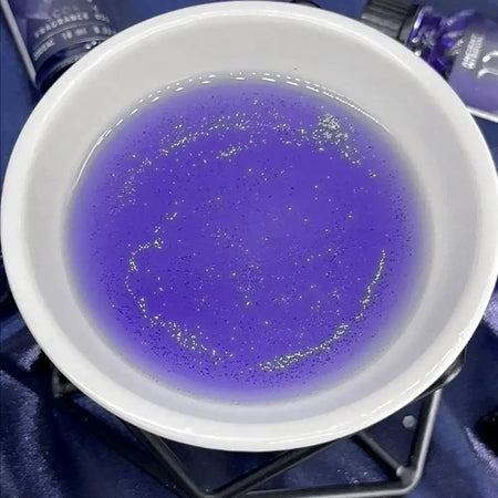 A white ceramic bowl holds zodiac fragrance oil aries 10ml with shimmering purple liquid and fine silver glitter particles